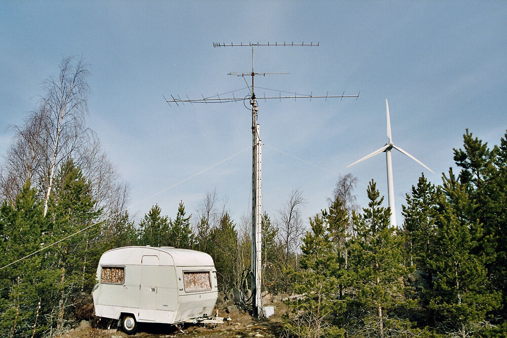 Portable amateur radio field setup with a telescopic mast and stacked Yagi antennas beside a camping trailer