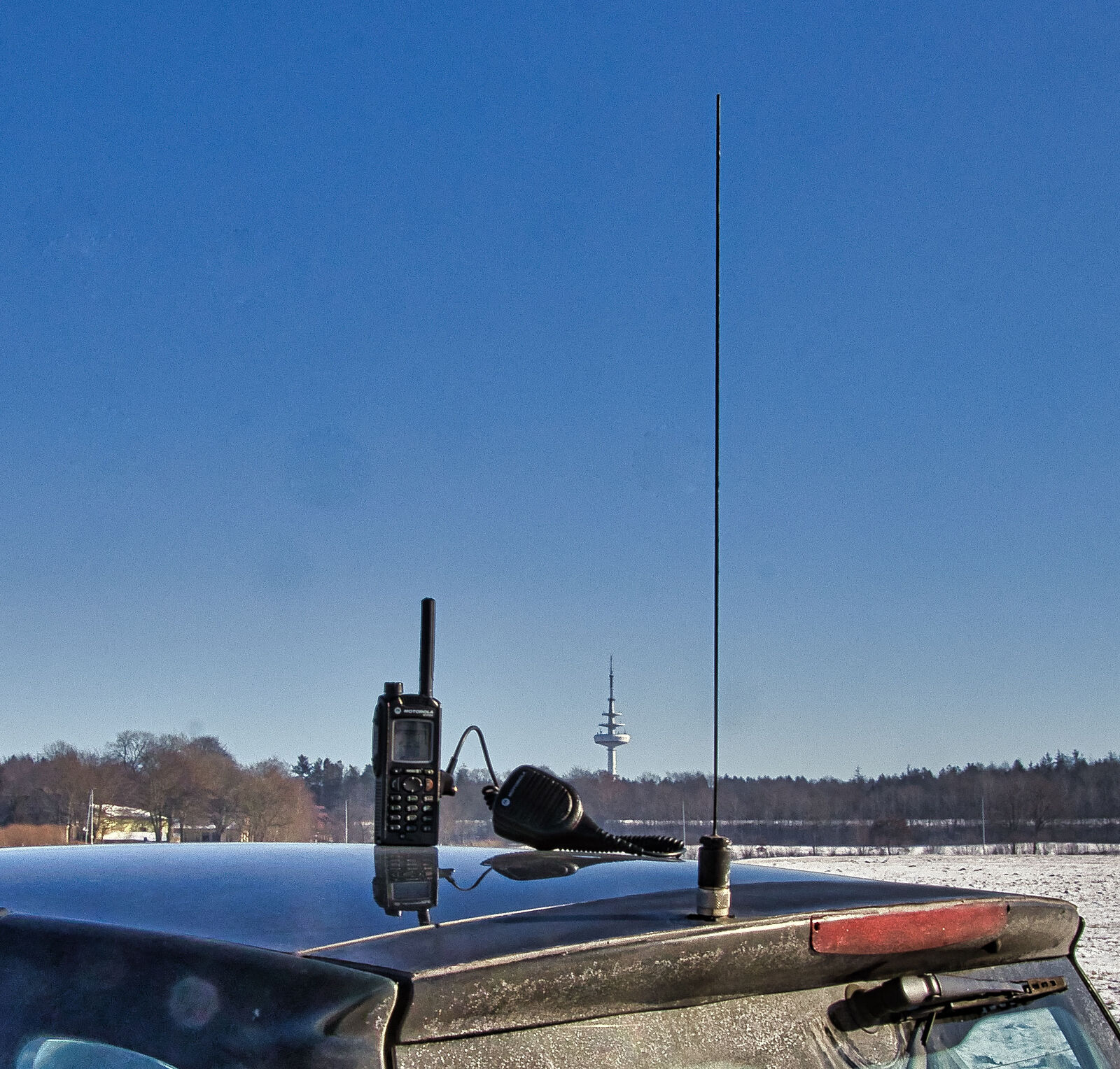 Dual-band VHF/UHF whip antenna on a vehicle roof mount with a handheld radio resting beside it