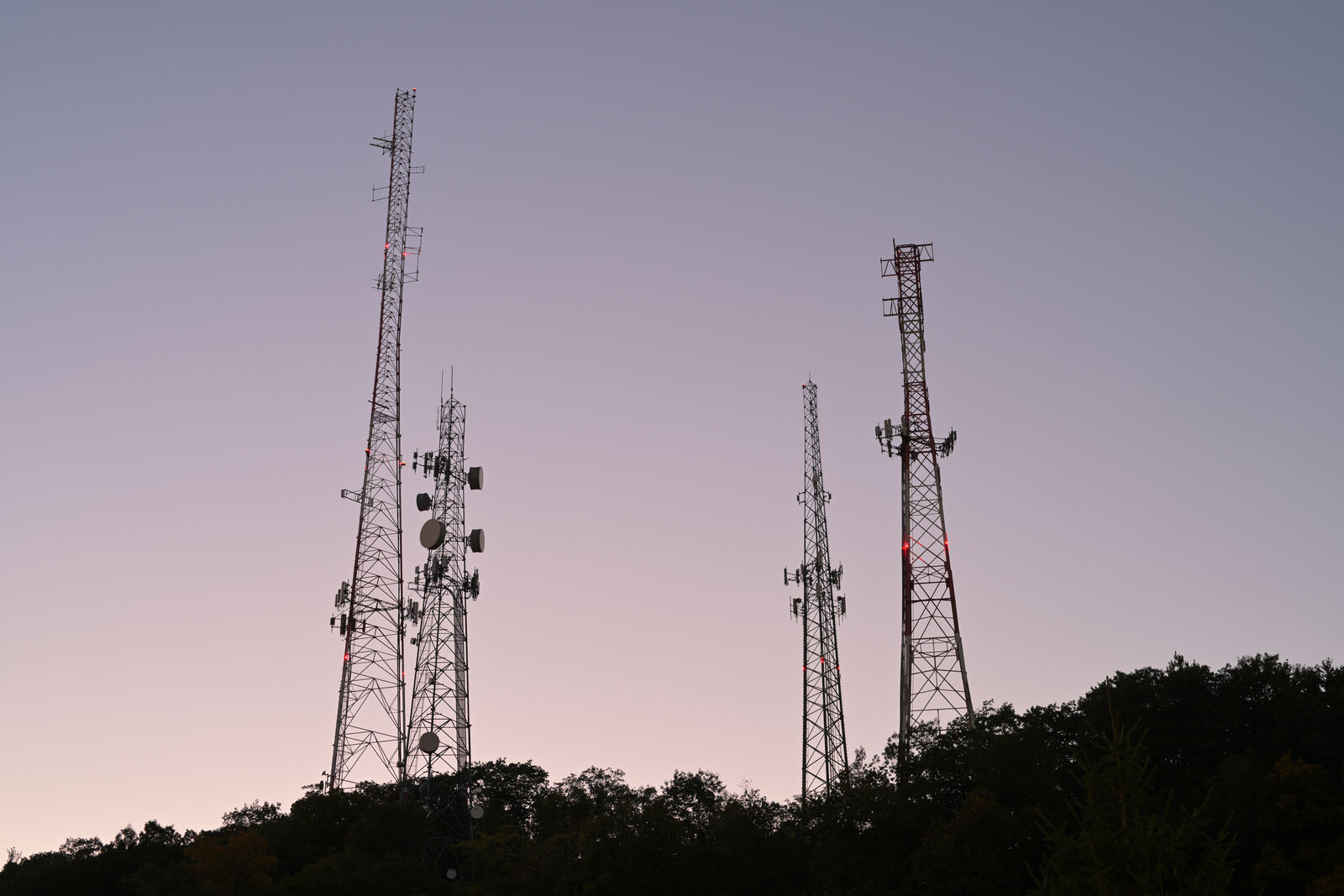 Radio and repeater towers silhouetted on a wooded hilltop against a dusk sky