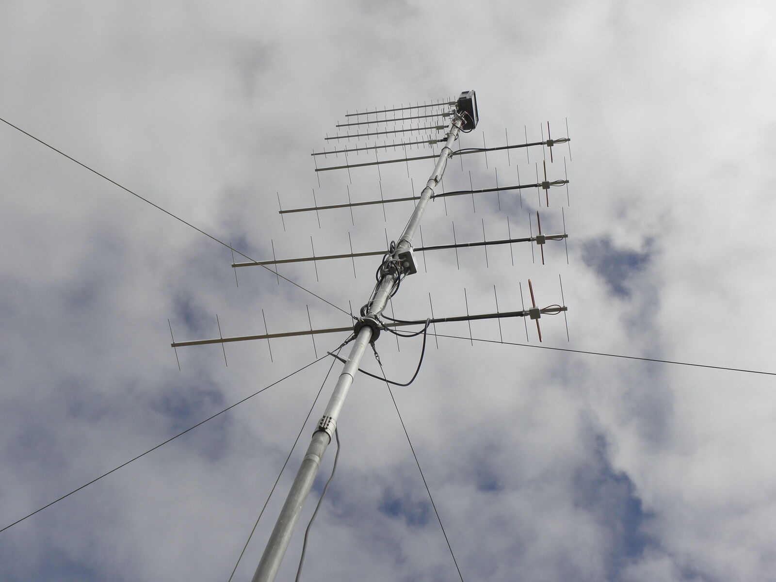 Guyed antenna mast with stacked VHF and UHF Yagi antennas photographed against a blue sky